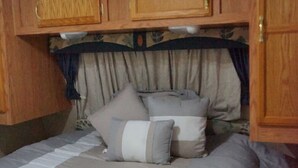 A bedroom with a bed, pillows, and wooden cabinets. - Camper in Dandridge. Close to the Smoky Mountains and Dollywood  (Dandridge)