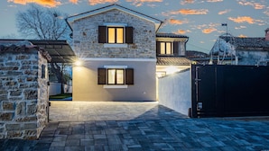 A two-story stone house with a paved driveway and a gated entrance.
