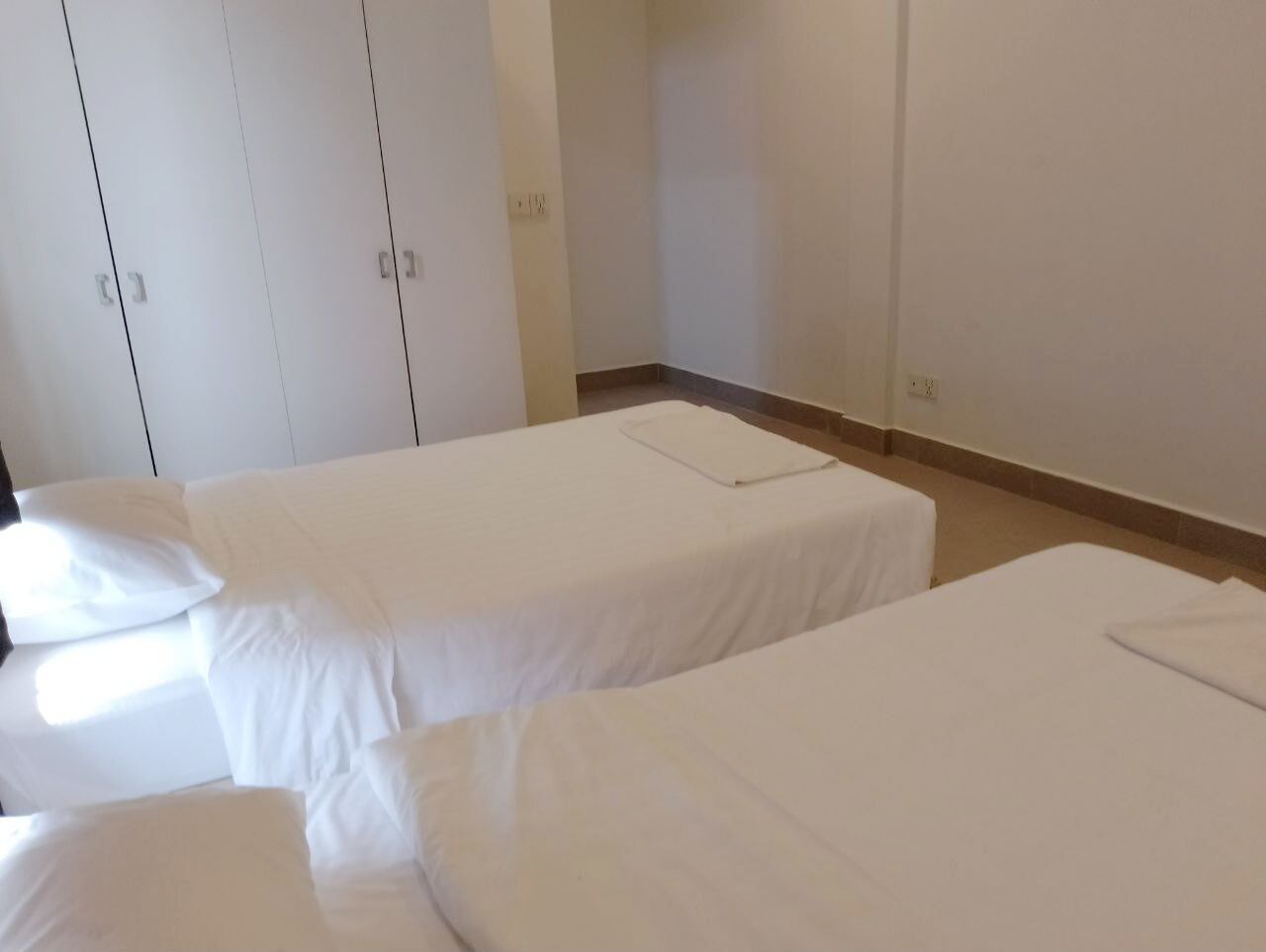 A room with three single beds, white bedding, and a plain wall with a door.