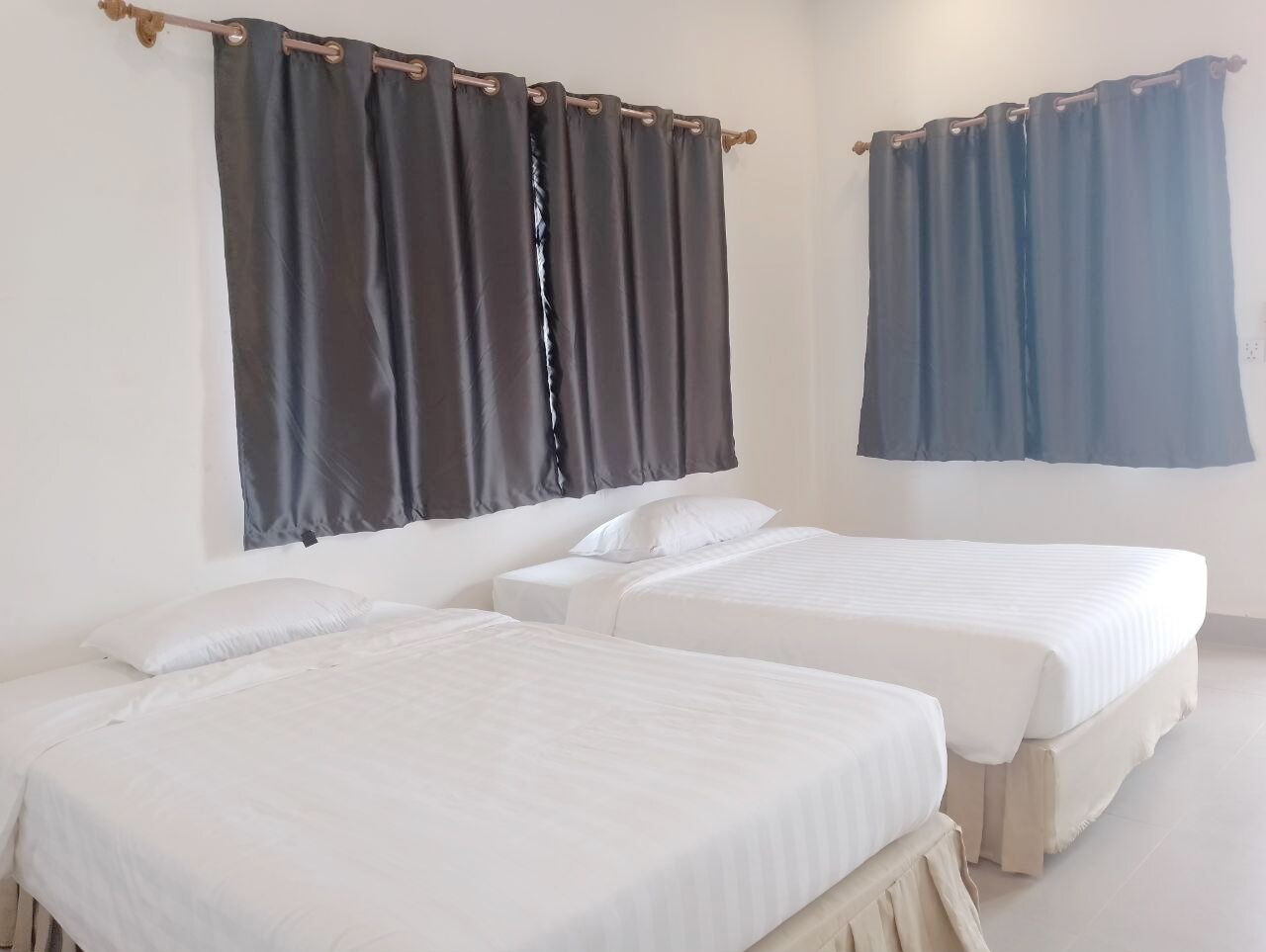A room with two single beds, white bedding, and dark curtains.