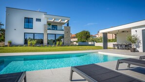 Una moderna casa a due piani con piscina, area salotto esterna e prato curato.