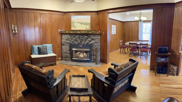 A cozy living room with a stone fireplace, wooden paneling, a dining area, and a bookshelf. - McKeever Lodge (Forestport)