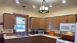 A kitchen with wooden cabinets, a sink, a microwave, a stove, and a window with blinds. - McKeever Lodge (Forestport)
