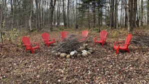 A forest clearing with six red Adirondack chairs arranged around a central fire pit. - McKeever Lodge (Forestport)