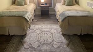 A room with two beds, a nightstand with a lamp, and a patterned rug.