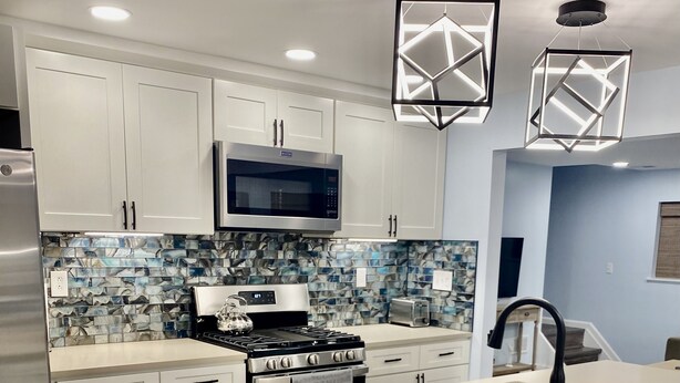A modern kitchen with white cabinets, a stainless steel stove, and a microwave. There are two pendant lights above the island.