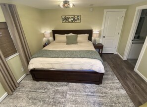 Een slaapkamer met een groot bed, twee nachtkastjes met lampen, een wandklok en een deur aan de rechterkant.