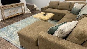 A living room with a sectional sofa, a coffee table, a TV on a wooden stand, and a staircase leading upstairs.