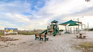 A beach playground with a slide, benches, and a picnic table.