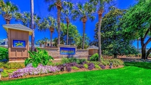 A hotel entrance with a sign reading "Ocean Lakes," surrounded by lush greenery and palm trees.