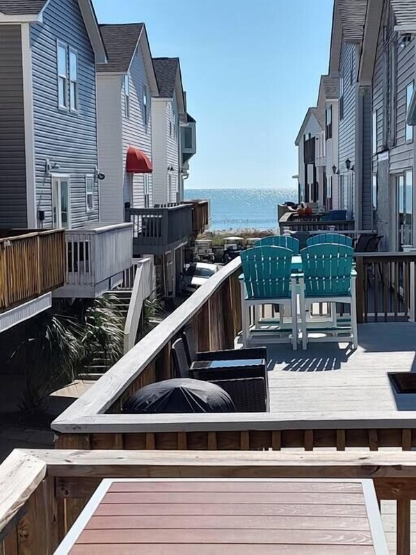 Terraza de madera con mobiliario exterior, con vista a la playa.