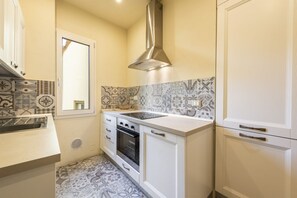 A kitchen with patterned tiles, a stainless steel range hood, a built-in oven, and white cabinetry.