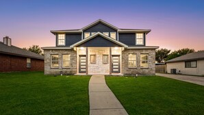 A two-story house with a stone facade, a central entrance with a stone archway, and a well-maintained lawn.