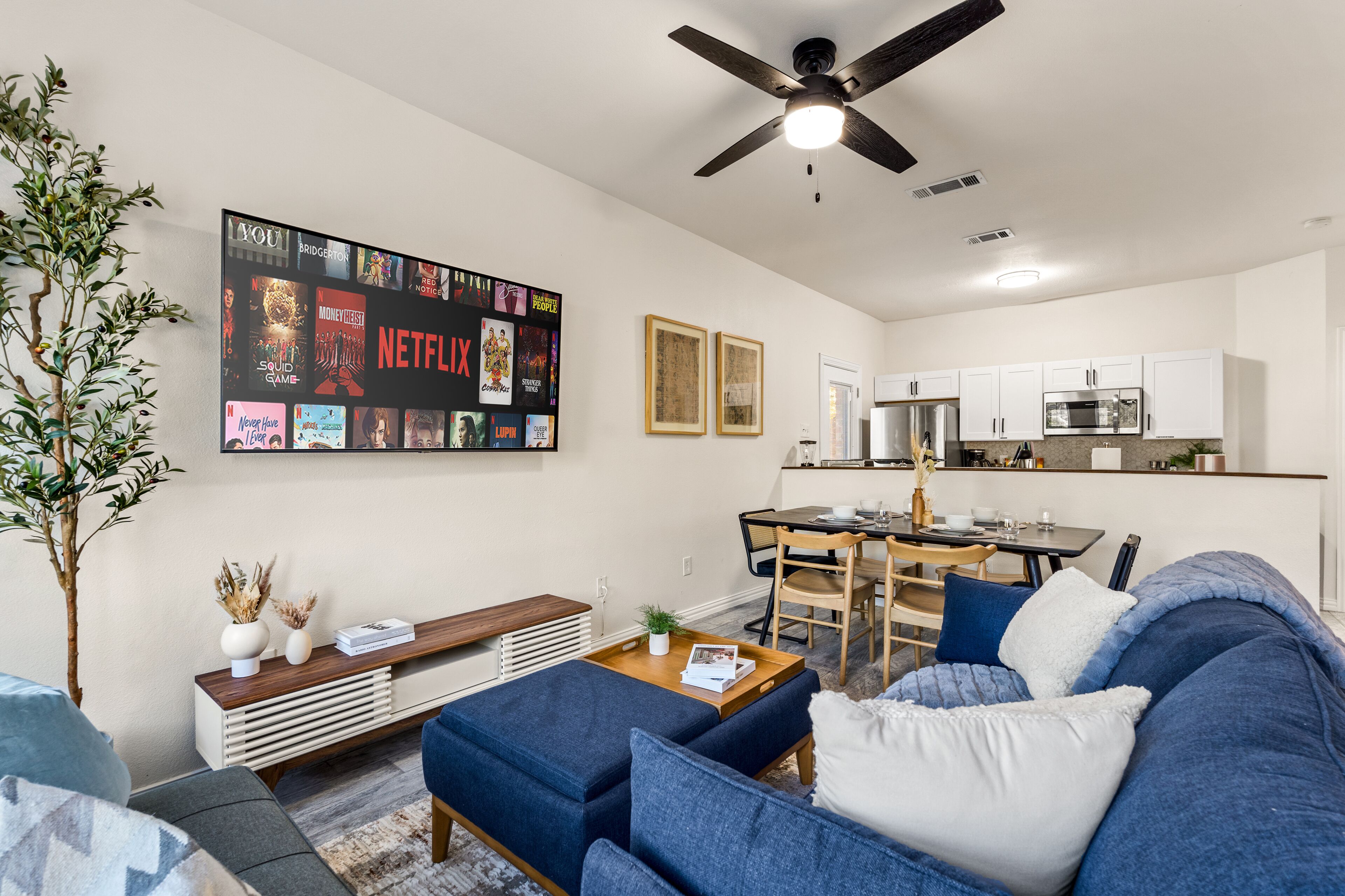 A modern living room with a blue sofa, a coffee table, and a TV wall art displaying various shows.