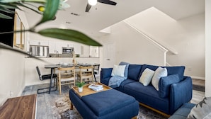 A modern living room with a blue sofa, a wooden coffee table, and a dining area with a table and chairs.