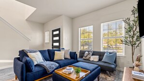 A modern living room with a sectional sofa, a wooden coffee table, and large windows with blinds.