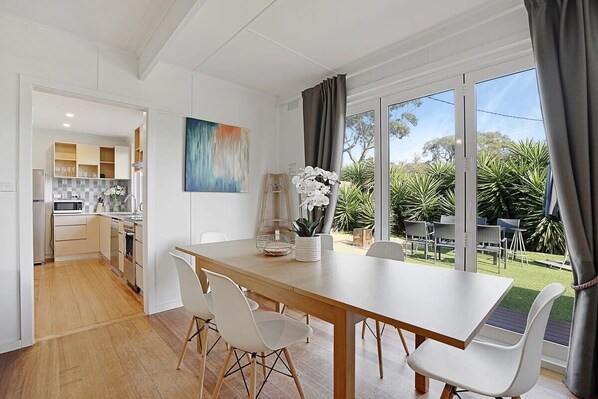 A modern kitchen with white cabinets, a wooden countertop, and a dining area with a large table and white chairs. - The Starfish Cottage - 250m to bay beach (Rye)