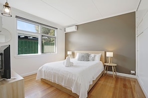 A bedroom with a large bed, bedside lamps, a TV, and a window with a view of a green fence. - The Starfish Cottage - 250m to bay beach (Rye)