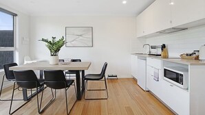 A modern kitchen with white cabinets, a dining table with chairs, a potted plant, and a microwave.