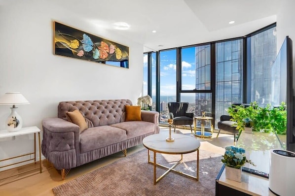 A modern living room with a tufted sofa, a round coffee table, and a large window offering a city view.