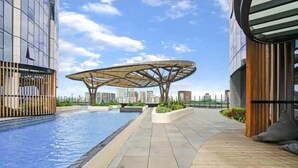 Um edifício moderno com piscina no terraço, uma estrutura circular singular e vista para o horizonte urbano.
