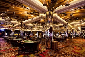 Un casino espacioso con varias mesas de blackjack, una alfombra colorida y candelabros modernos.