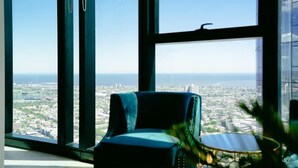 A room with large windows, a chair, and a small table. - Breathtaking Views 49th floor - Melbourne Square (Southbank)