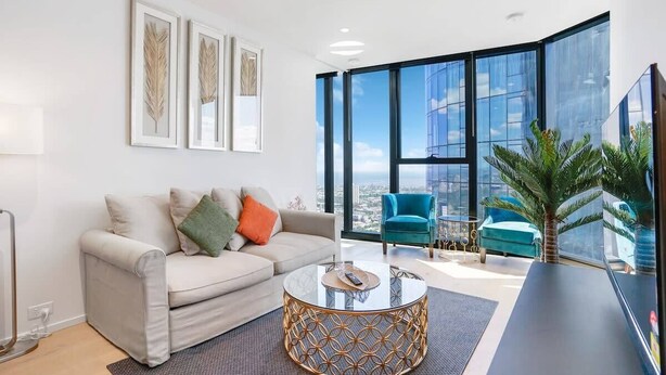 A modern living room with a sofa, a coffee table, and a large window offering a city view. - Breathtaking Views 49th floor - Melbourne Square (Southbank)