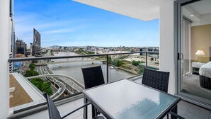 A balcony with a table and chairs, overlooking a cityscape with a river and modern buildings.