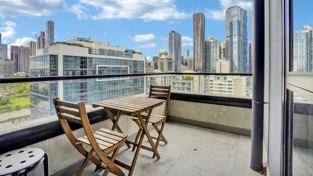 Un balcón con mesa y sillas, con vista a un paisaje urbano de edificios modernos.
