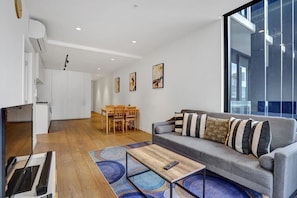 Ein modernes Wohnzimmer mit grauem Sofa, einem Holztisch als Couchtisch und einem Essbereich mit Holztisch und Stühlen.