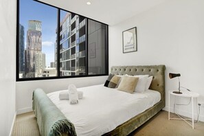 A modern bedroom with a large window, a tufted headboard, and a view of a cityscape.