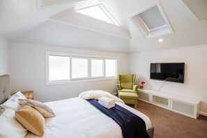 Un dormitorio con una cama grande, televisión, tragaluz y ventana.