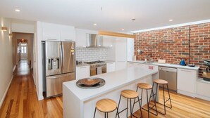 A modern kitchen with a central island, stainless steel appliances, and a brick accent wall. - SENSATIONAL Renovated Cottage in Beautiful Seddon (Seddon)
