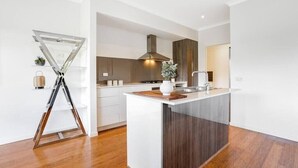 A modern kitchen with a central island, wooden flooring, and a visible stove. - Bundoora Family Home near Uni Hill (Bundoora)