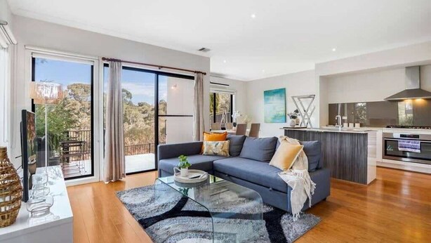 A modern living room with a sofa, coffee table, and a view through large sliding doors to an outdoor area. - Bundoora Family Home near Uni Hill (Bundoora)