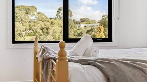 A bedroom with a bed, a window with a view of trees and a building, and a wooden headboard. - Bundoora Family Home near Uni Hill (Bundoora)