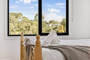A bedroom with a large window offering a view of trees and a building.