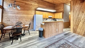 Un interior de madera con una mesa de comedor, sillas, una zona de cocina con armarios, un refrigerador y un cubo de basura.
