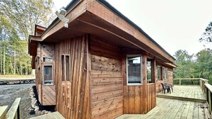 Una cabaña de madera con un balcón, ventanas amplias y vistas al bosque circundante.