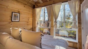 Acogedora habitación de cabaña de madera con cama, ventilador de techo y ventana con cortinas.