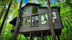 Una casa en los árboles con varias ventanas y un balcón, rodeada de un bosque.