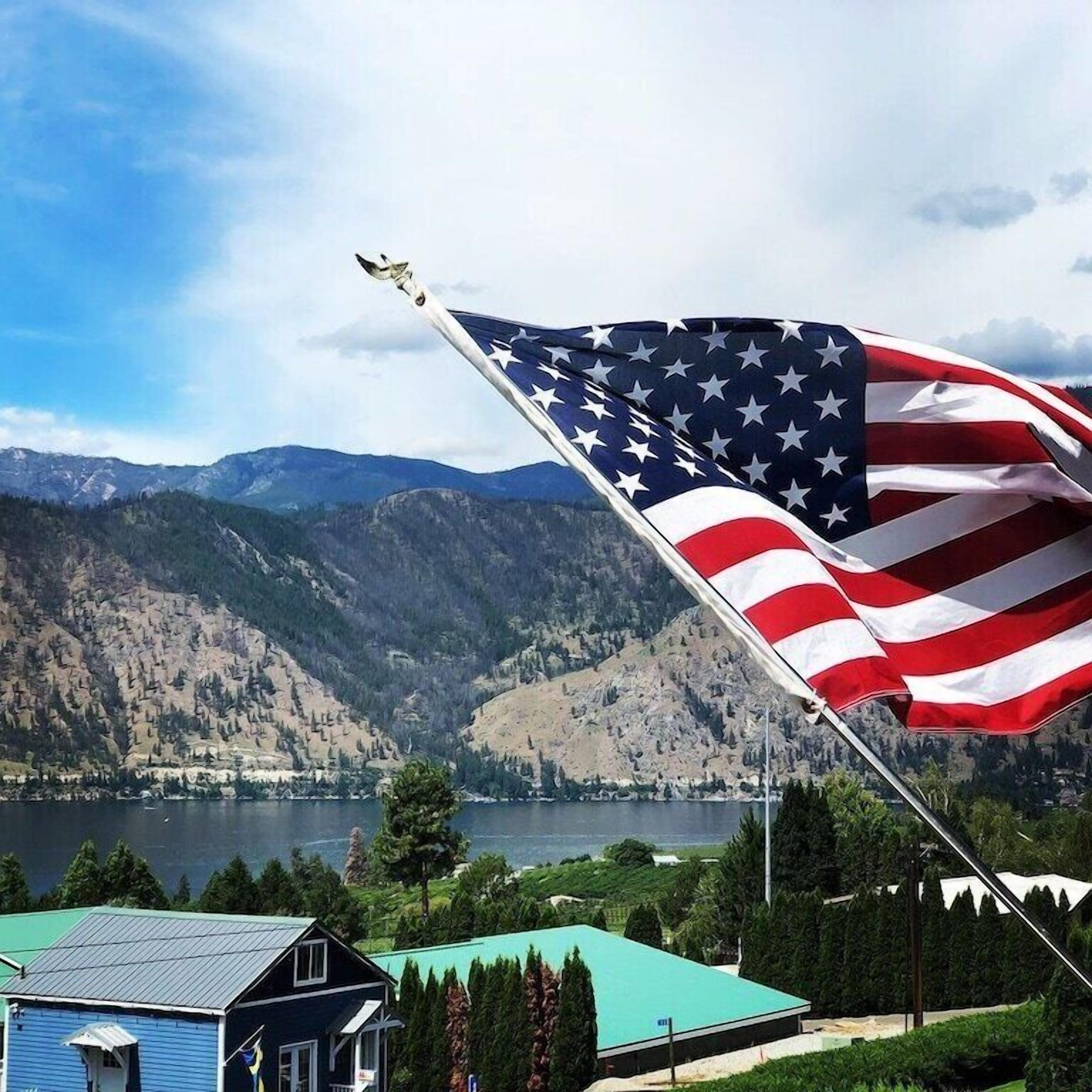 Eine Fahnenstange mit einer amerikanischen Flagge vor einer Berglandschaft und einem Gewässer.