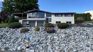 Una moderna casa a due piani con un ampio garage, immersa in un paesaggio roccioso e un idrante in primo piano.