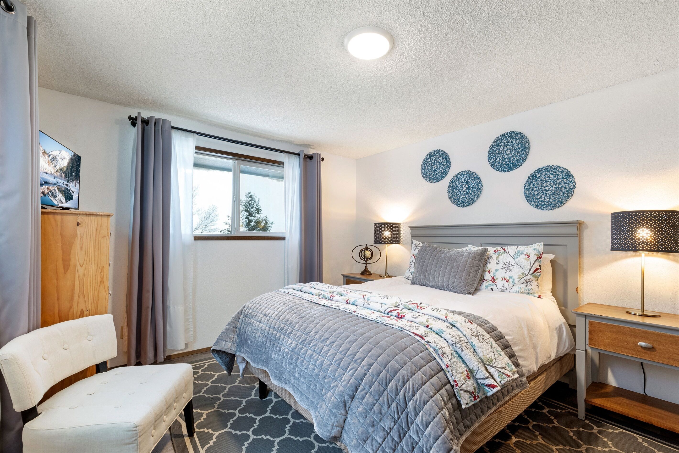 A bedroom with a bed, bedside tables, a chair, a wardrobe, and a window with curtains.