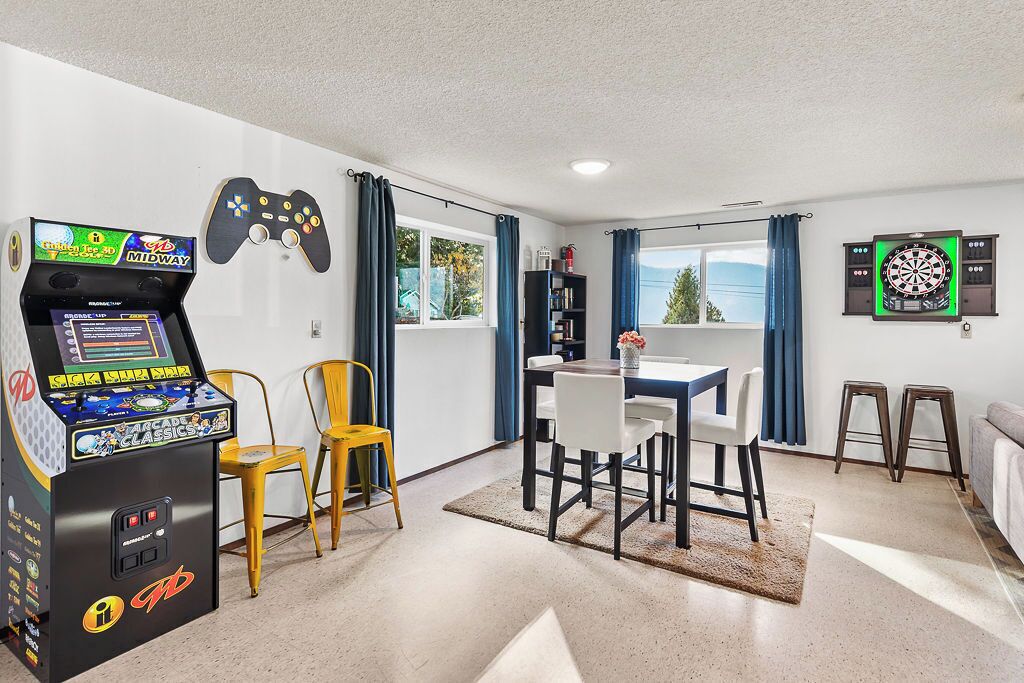 Une pièce équipée d’une console de jeux, d’un jeu de fléchettes, d’une table avec des chaises et offrant une vue sur l’extérieur.