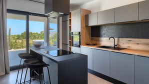 Una cocina moderna con una isla central, taburetes de bar y vistas al exterior.