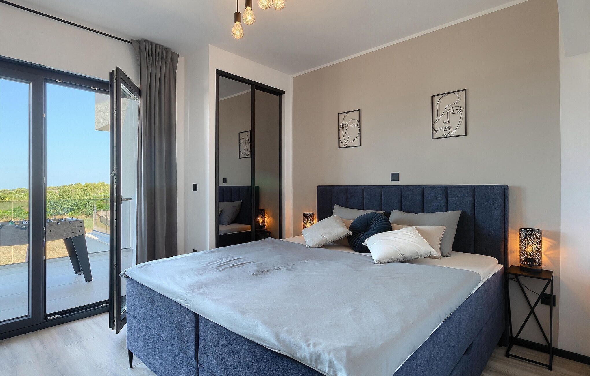 A modern bedroom with a large bed, a sliding glass door to a balcony, and two wall-mounted picture frames.