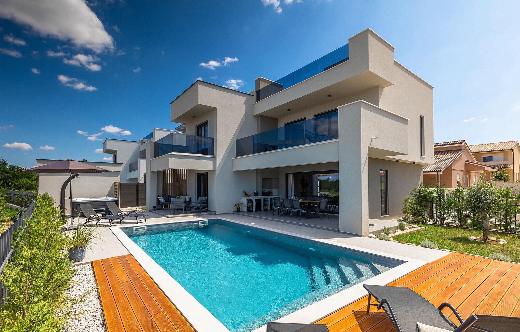 Una casa moderna de dos pisos amb piscina, zona d'estar a l'exterior i jardí ben cuidat.