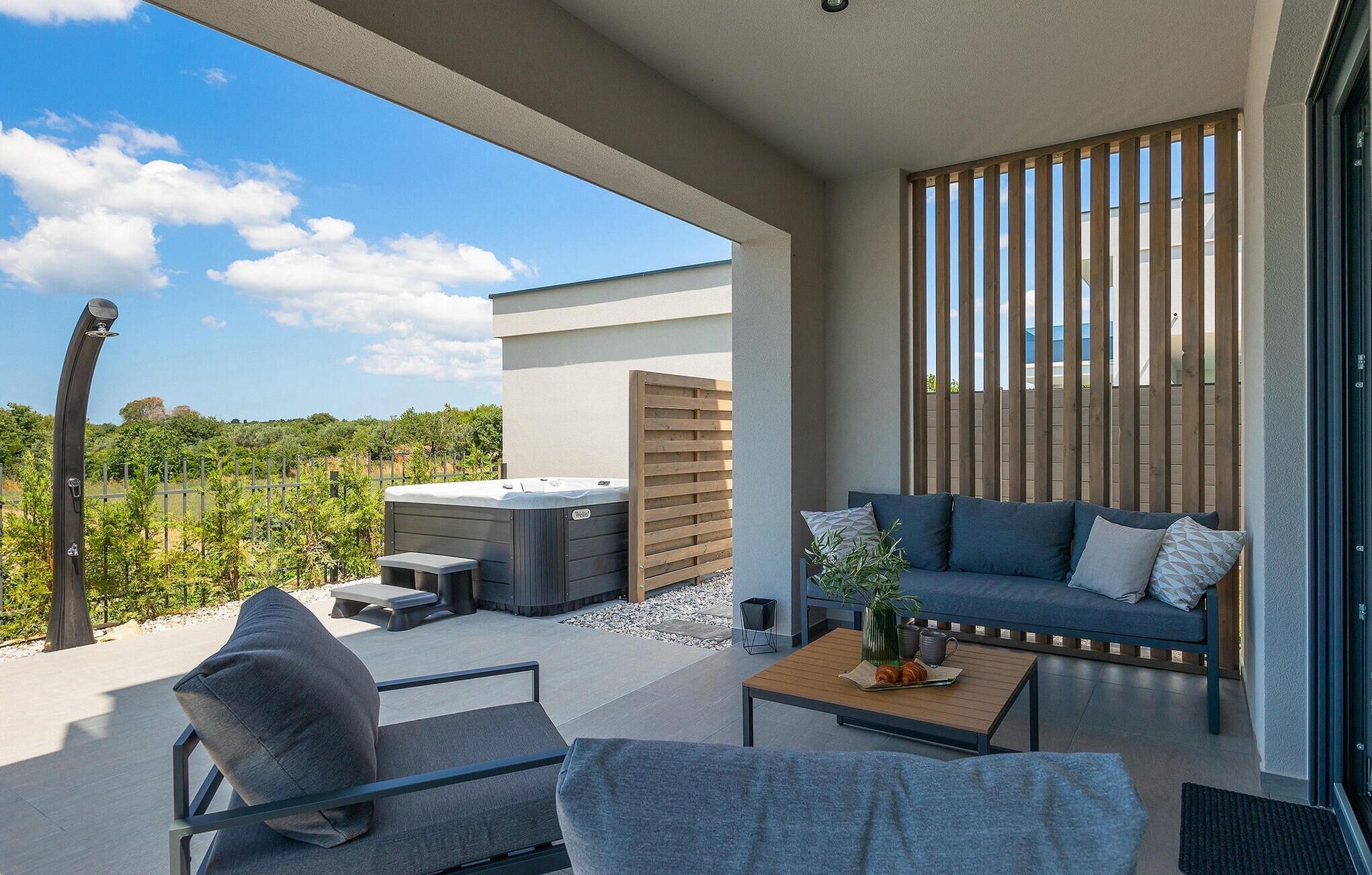 A modern outdoor patio with a sofa, chairs, and a hot tub.